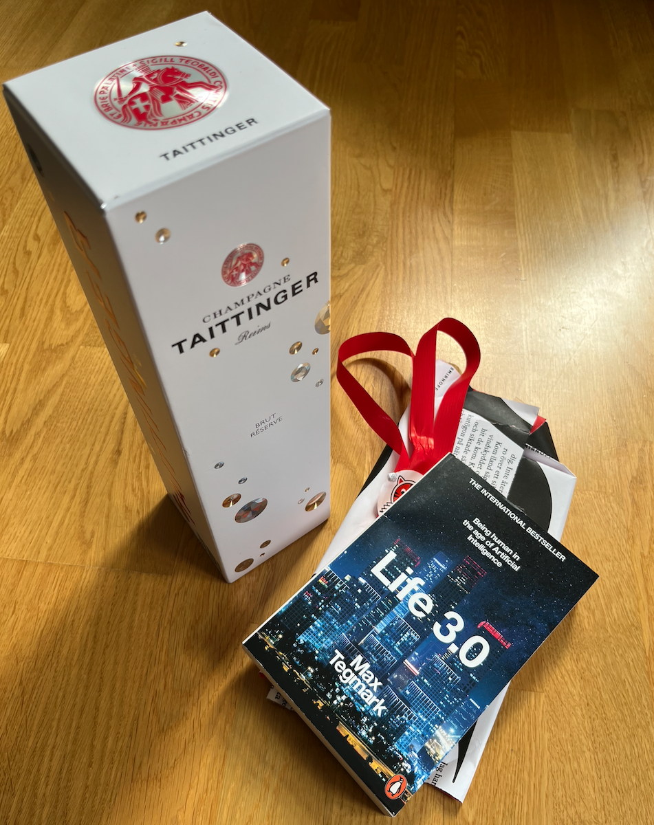 A bottle Taittinger champagne along with a book - 'Life 3.0' by Max Tegmark
